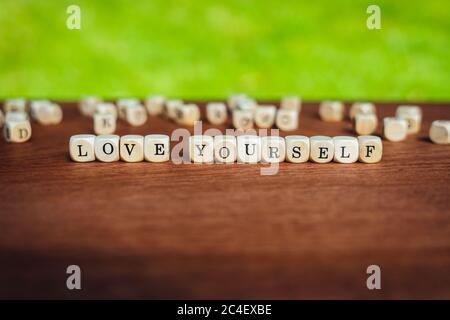 Nahaufnahme von isolierten Würfel auf einem Tisch, der die Worte Liebe dich vor einem gesättigten Hintergrund zeigt Stockfoto