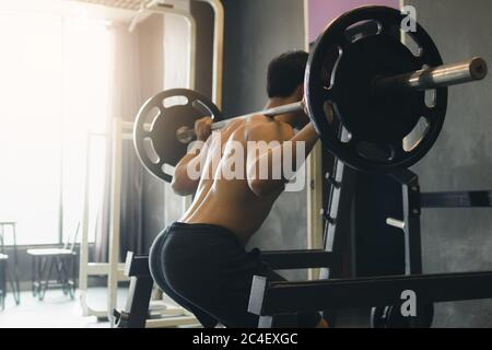 Rückansicht des asiatischen Mannes Durchführung Langhantel hockt im Indoor-Fitness-Studio. Stockfoto