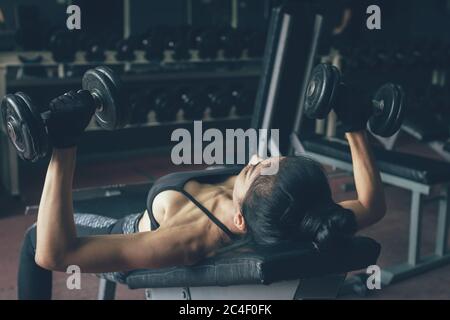 Schöne asiatische Frau Heben Gewichte Hantel für ihre Brust in der Nähe Fenster im Fitnessstudio innen. Stockfoto