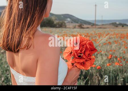 Braut in einem weißen Kleid mit einem Bouquet von Mohnblumen, warme Sonnenuntergangszeit auf dem Hintergrund des roten Mohnfeldes. Speicherplatz kopieren. Das Konzept von Stockfoto