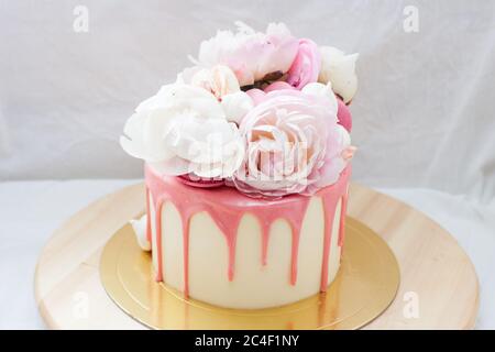 Kleine Geburtstagstorte mit geschmolzener rosa Schokolade, frischen Blumen, Makronen und Baisenkuchen auf weißem Hintergrund. Stockfoto