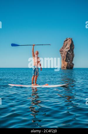 Stand Up Paddle Boarding. Sportler Mann posiert auf einem SUP-Board. Das Abenteuer des Meeres mit blauem Wasser auf einem Surfen. Das Konzept eines aktiven und Stockfoto