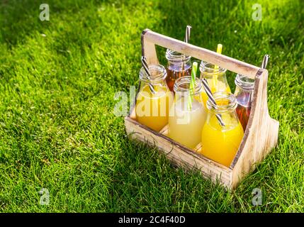 Sortiment von Limonade und Eistee in Flaschen in Holzgestell im Gras Stockfoto