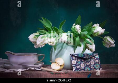 Klassisches Stillleben mit weißen Tulpen, einem halben Apfel und einem Umschlag auf altem Holztisch auf grünem Hintergrund Stockfoto