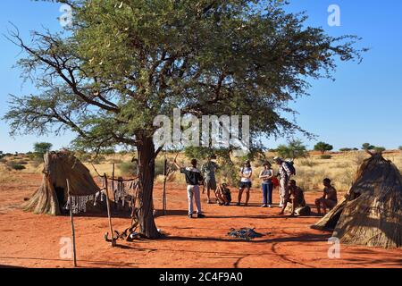 KALAHARI, NAMIBIA - 24. JAN 2016: Touristen besuchen das Dorf der Buschmänner. Die San, auch Buschmänner genannt, sind Mitglieder verschiedener indigener Jäger Stockfoto