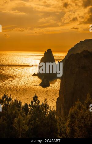 Ein rot brennender Sonnenuntergang mit dem Silhouett einer Klippe über dem Meer Stockfoto