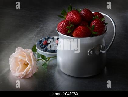Erdbeeren in Aluminiumdose, Rose und Geißblatt auf silberner Oberfläche, Stillleben Stockfoto