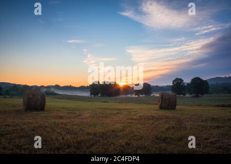 Heuballen rollten auf dem Feld bei Sonnenaufgang mit Nebel schafft erstaunliche Himmel im Frühsommer Sussex County NJ Stockfoto