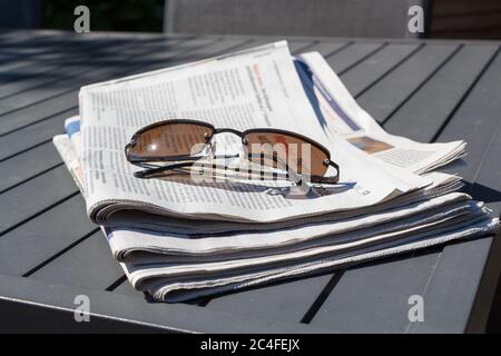 Stapel von Zeitungen und Sonnenbrillen auf einem Tisch im Garten Stockfoto