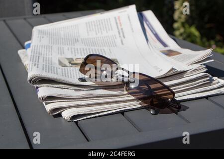 PRIMELIN - FRANKREICH, JULI 11 : Stapel von Zeitungen und Sonnenbrillen auf einem Tisch im Garten, 11. Juli 2018 Stockfoto