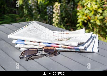 Stapel von Zeitungen und Sonnenbrillen auf einem Tisch im Garten Stockfoto