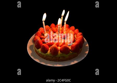 Erdbeer-Geburtstagstorte von vier Kerzen isoliert auf schwarzem Hintergrund beleuchtet. Stockfoto