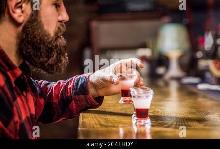 Bärtiger Mann in pab. Bärtiger Mann Schüsse Cocktail. Tequila-Schuss. Bunte Cocktails an der Bar. Tequila Shots, Wodka, Whisky, Rum. Alkohol trinken in Stockfoto