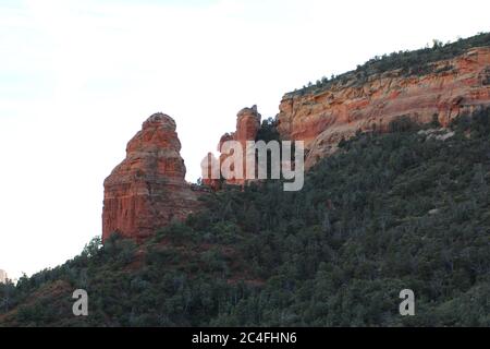 Hoch aufragende rote Sandsteinfelsen und schiere Klippen führen zu abfallenden Canyon Wände mit immergrünen Bäumen auf dem Brins Mesa Trail in Sedona, A gefüllt Stockfoto