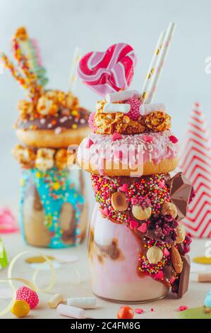 Valentinstag Konzept. Himbeer-Freak Shake Topping mit Donut, Karamell Popcorn und Süßigkeiten auf Party-Hintergrund. Selektiver Fokus. Stockfoto