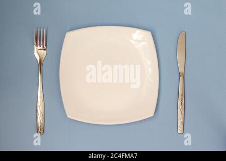 Leere Platte, Gabel, Messer auf blauem Hintergrund. Teller und Besteck reinigen. Stockfoto