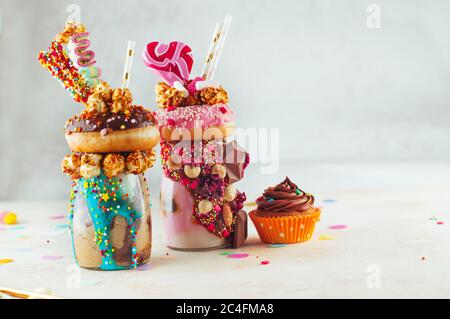 Zwei Freak-Shakes mit Donuts, Popcorn und Süßigkeiten auf Party-Hintergrund. Selektiver Fokus. Stockfoto