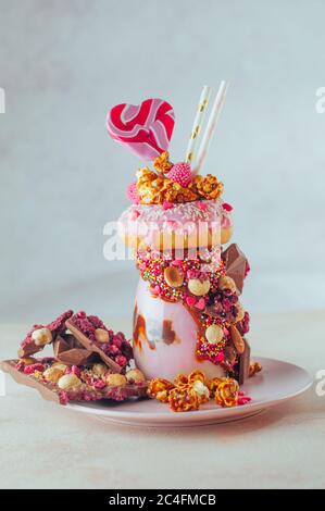 Valentinstag Himbeer-Freak-Shake Belag mit Donut, Karamell Popcorn und Süßigkeiten auf beigem Hintergrund. Selektiver Fokus. Stockfoto