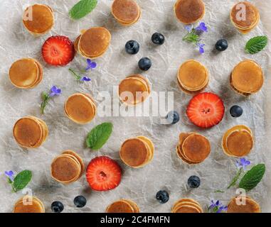 Süße hausgemachte kleine Pfannkuchen mit Erdbeeren und Heidelbeeren auf weißem Pergamentpapier.Food Hintergrund. Flach liegend. Horizontal. Stockfoto