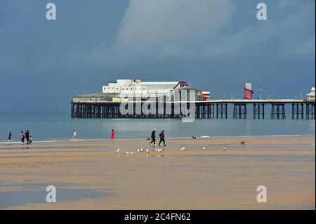 Ein Paar zu Fuß Hund am Strand und Menschen am Wasser Rand unter stürmischen Bedingungen, Blackpool, Großbritannien Stockfoto
