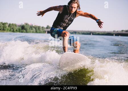 Ein Mann surft auf einem Surfbrett, das von einem Motorboot über der Welle des Bootes gezogen wird. Weixerfer beschäftigt sich mit Surfen, Unterhaltung, Freizeit, Wasser Stockfoto