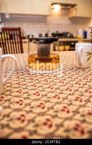 Glaspudding mit Tee und Tassen auf dem Küchentisch im Hintergrund der Küche. Für Text platzieren. Das Konzept des glücklichen Familienlebens. Stockfoto