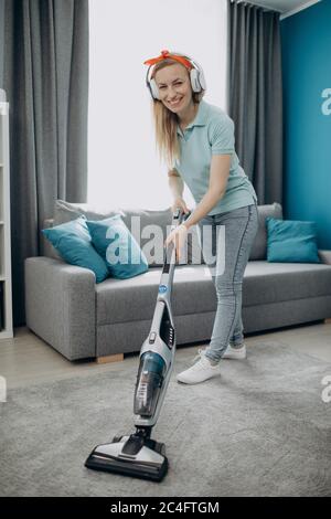 Glückliche Frau in Kopfhörer, die Teppich im gemütlichen Zimmer saugt Stockfoto