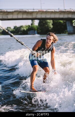 Ein Mann surft auf einem Surfbrett, das von einem Motorboot über der Welle des Bootes gezogen wird. Weixerfer beschäftigt sich mit Surfen, Unterhaltung, Freizeit, Wasser Stockfoto