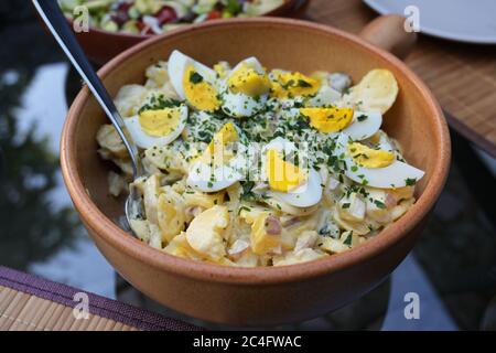 Kartoffelsalat mit gekochten Eiern und Kräutern garnieren in einer rustikalen Schüssel auf einem Glas Gartentisch, ausgewählte Fokus enge Schärfentiefe Stockfoto