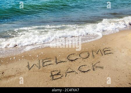 Worte Willkommen Zurück sind in den Sand am Strand in der Nähe des Wassers geschrieben, wieder nach der Coronavirus Pandemie, sind Ferien auf See wieder möglich für tou Stockfoto