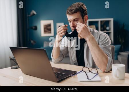 Serious Kerl arbeiten auf Laptop in schützende medizinische Maske Stockfoto