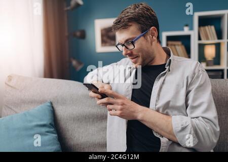 Schöner Mann, der sich auf der Couch entspannt und das Smartphone benutzt Stockfoto