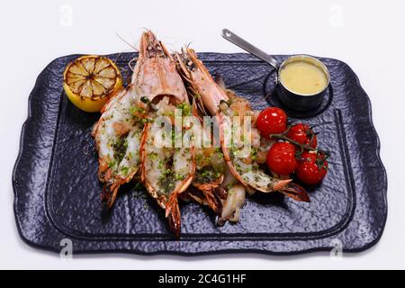 Gegrillte Tigergarnelen mit Zitrone und Kirschtomate auf einem schwarzen Teller Stockfoto