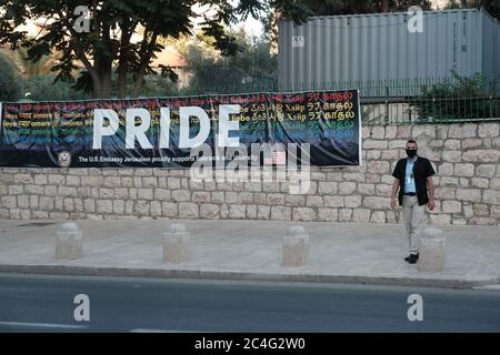 Jerusalem, ISRAEL 26. Juni 2020: Ein Sicherheitsmann steht neben einem Banner, das den LGBTQ Pride Month feiert und auf dem stand: „STOLZ: Die US-Botschaft Jerusalem unterstützt stolz Toleranz und Vielfalt“, der vor der Wand des US-Konsulats in Jerusalem aufgehängt wurde, obwohl Stadtbeamte seine Entfernung forderten. Das Konsulatsgebäude steht vor einem Park, in dem die lokale LGBTQ-Gemeinde ihre jährliche Pride-Kundgebung abhält. Quelle: Eddie Gerald/Alamy Live News Stockfoto