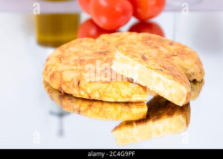 Nahaufnahme eines schmackhaft aussehenden spanischen Omelettes mit einer Scheibe, die auf einem Glastisch mit einigen unscharf Tomaten im Hintergrund herausgenommen wurde. Spanisch und trad Stockfoto