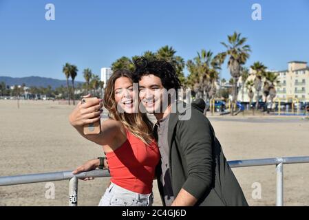 Junges Paar, das am Strand in einem tropischen Ferienort Handyfotos von sich selbst gemacht hat Stockfoto