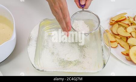 Zubereitung von Biskuit-Teig. Frau verteilt Butter und Mehl über die Seiten der Glasbackform. Stockfoto