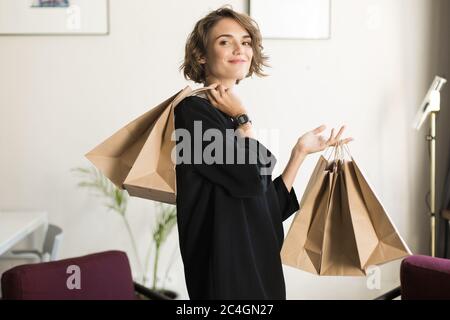 Junge hübsche lächelnde Frau mit kurzen lockigen Haaren in schwarzem Kleid Stockfoto
