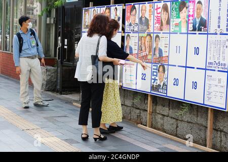 Menschen mit Gesichtsmasken sehen sich Poster von Kandidaten bei den bevorstehenden Gouverneurswahlen in Tokio an. Es liegt auf einem Gehweg in Ginza. Stockfoto