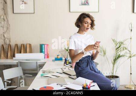 Junge Frau mit kurzen lockigen Haaren in kabellosen Ohrhörern sitzend Stockfoto