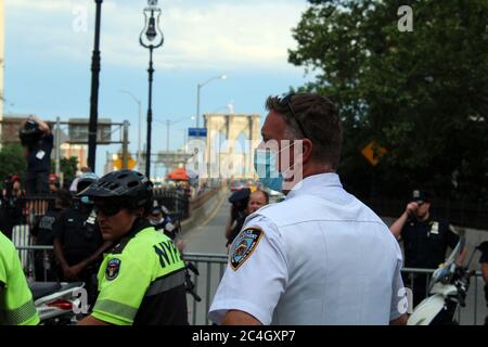 25. Juni 2020, New York, New York, USA: Nach wochenlangen Protesten gegen Polizeibrutalität und Rassenungerecht zelten Demonstranten in New York City vor dem Rathaus, um eine Milliarde Dollar an Kürzungen für die Finanzierung der NYPD zu fordern, bevor die Stadt am 1. Juli ihre Budgetfrist erreicht hat. Dieser maskierte NYPD-Polizist steht mit einer Truppe vor der Brooklyn Bridge neben dem Protestlager, das kurz vor dem Beginn eines marsches steht. Befürworter der Polizeireform sagen, dass das fast 6 Milliarden Dollar schwere Polizeibudget der Stadt deutlich gekürzt und in Wohnungen, Gesundheitsversorgung und andere soziale Dienste reinvestiert werden muss. (Bild: © Stockfoto