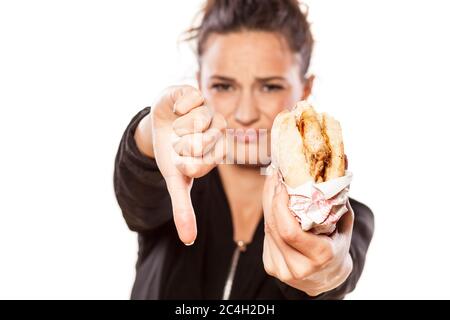Mädchen hält ein Sandwich und zeigt Daumen nach unten auf weißem Hintergrund Stockfoto