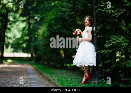 Brunette Braut in einem Kleid mit einem Brautstrauß im Park auf einem Hintergrund von Grün Stockfoto