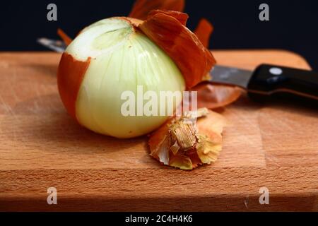 Zwiebeln werden mit einem Messer auf einem Holzbrett geschält Stockfoto