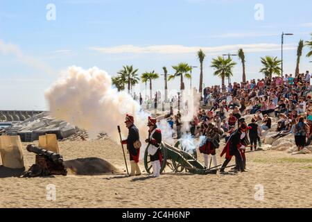 Malaga, Spanien - 26. Oktober 2014: französische Soldaten aus dem 18. Jahrhundert feuern eine Kanone mit Schießpulver. Männer und Frauen reenactors mit einer Menge hinter ihnen. Hist Stockfoto