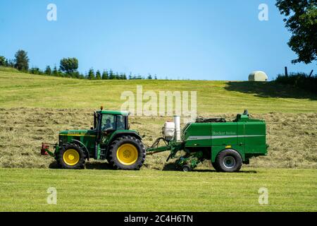 Heuernte, Landwirt mit landwirtschaftlicher Maschine, nimmt gemähtes Heu, das sofort in Ballen gepresst und in Folie verpackt wird, Ballenpresse / Wrapper combinati Stockfoto