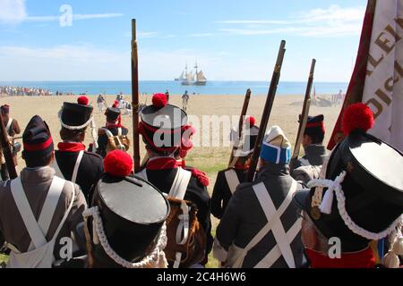 Malaga, Spanien - 26. Oktober 2014: Zug napoleonischer Soldaten in Formation mit Waffen und einer Flagge, von hinten gesehen. Vorne ist eine Brigg in der Nähe Stockfoto