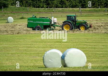 Heuernte, Landwirt mit landwirtschaftlicher Maschine, nimmt gemähtes Heu, das sofort in Ballen gepresst und in Folie verpackt wird, Ballenpresse / Wrapper combinati Stockfoto