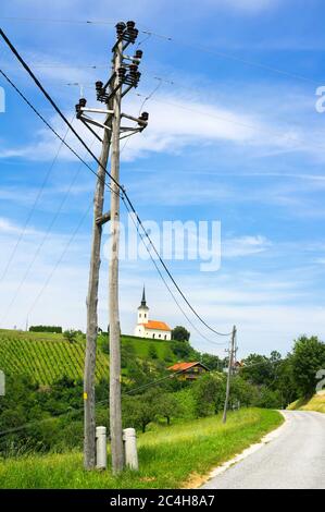 Sveti Urban, Nähe Maribor, Slowenien, Europa - Hügel mit Weinberg und kleine christliche Kirche auf der Spitze. Elektrischer Pol und Straße im Vordergrund Stockfoto