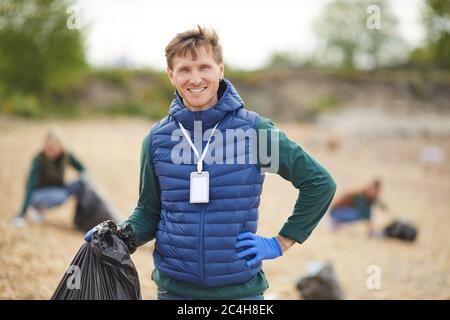 Porträt eines jungen Mannes, der im Freien steht und mit Müll in der Tasche hält und die Kamera lächelt Stockfoto